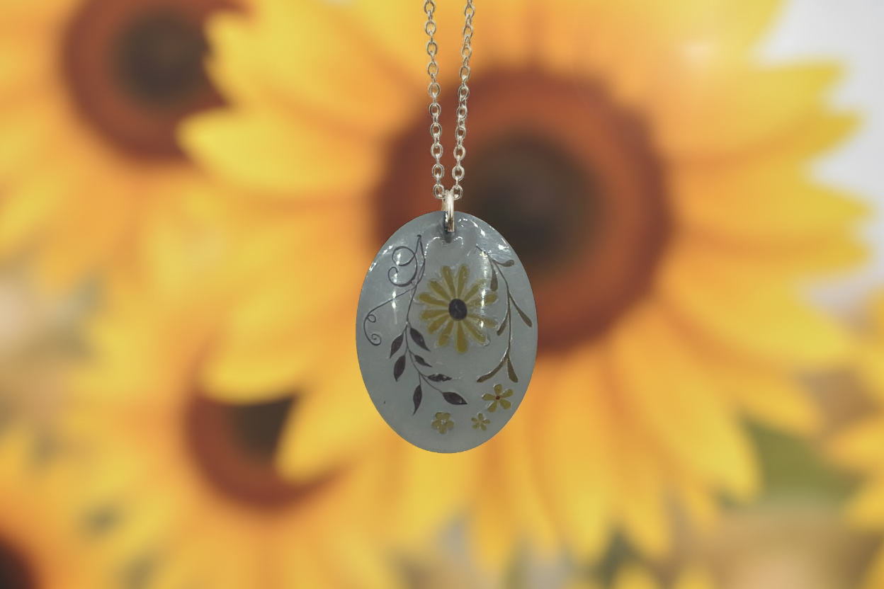 Necklace with a floral pendant in front of sunflowers